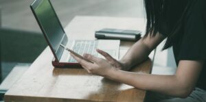 A young woman multitasking with her smartphone and laptop at a table indoors.